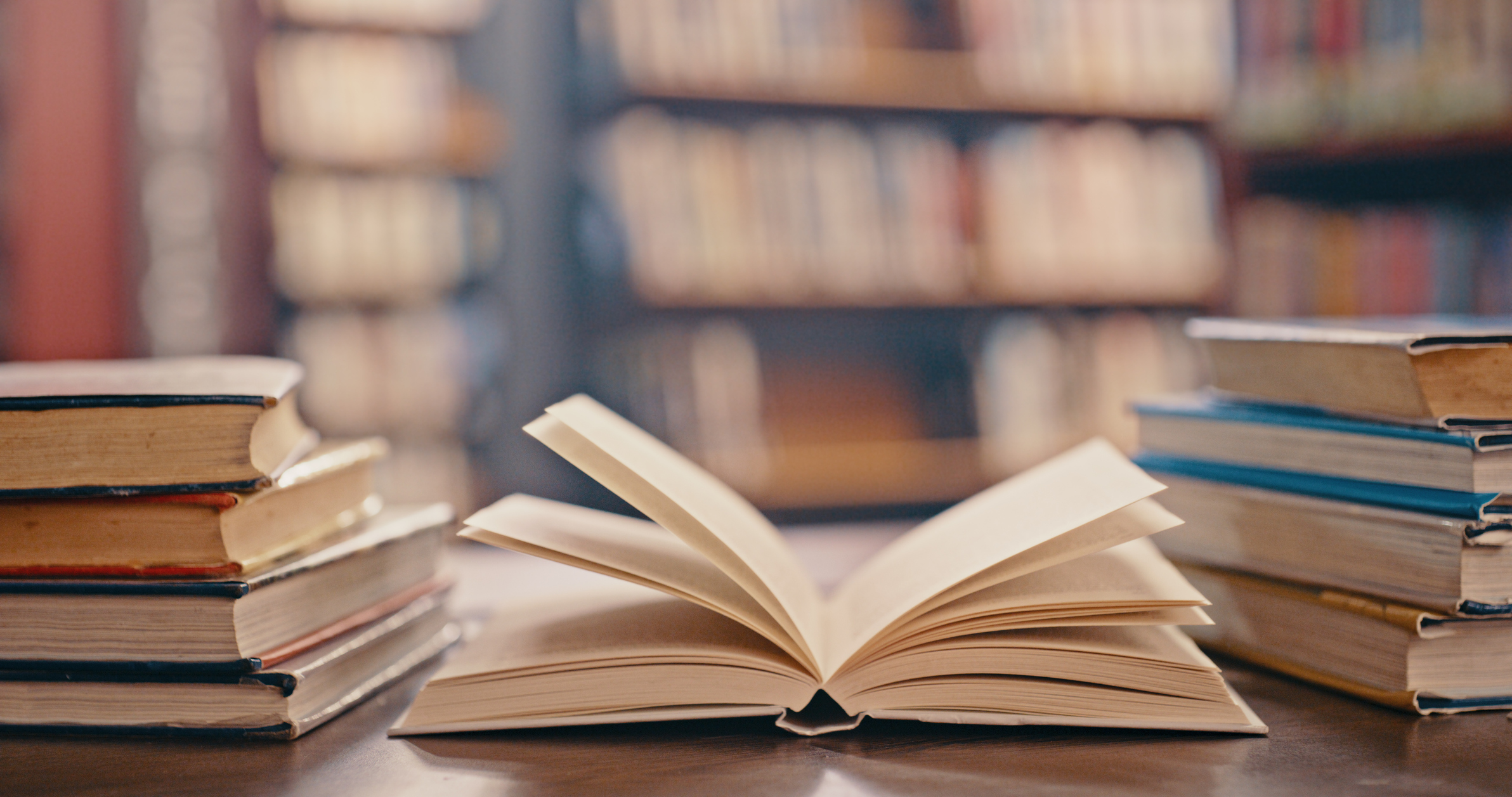 Library, books on table and background for studying, learning and research in education, school or college. Reading, philosophy and open, vintage or history print book, university blurred background AI e scuola, intervista a Mario Rasetti